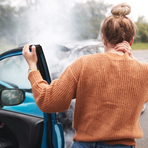 Rear View Of Female Motorist With Head Injury Getting Out Of Car After Crash